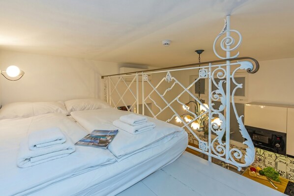 A hotel room with a bed, white linens, a magazine, a decorative metal railing, and a kitchen area with a microwave. - Tromostovje In Heart Of Ljubljana (Ljubljana)