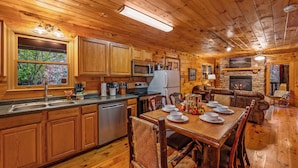 Cocina de cabaña de madera con una mesa de comedor, sillas, refrigerador, estufa, microondas y una chimenea de piedra.