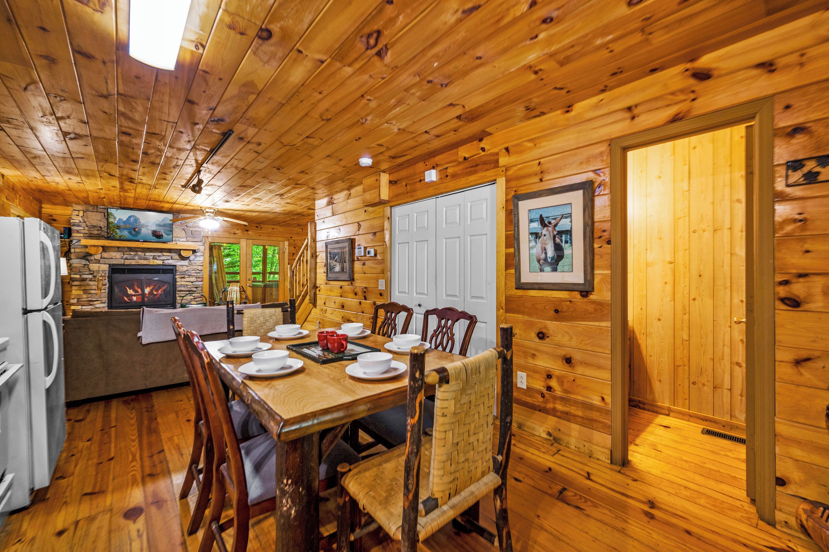 Ein Holzblockhaus-Interieur mit einem Esstisch für vier Personen, einem Steinkamin und einer Küchenzeile inklusive Kühlschrank.