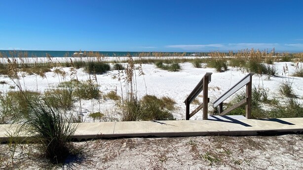 A beach with a concrete walkway leading to the water, surrounded by sand and sparse vegetation. - Gulf Front Vacation Rental- Anna Maria Island, Florida (Anna Maria)