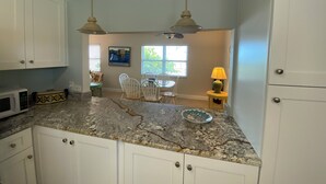 A kitchen with white cabinets, granite countertops, a dining area with chairs, a table, and a window with blinds. - Gulf Front Vacation Rental- Anna Maria Island, Florida (Anna Maria)