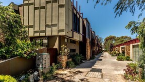 Un bâtiment moderne avec une façade en briques, une allée couverte et une végétation luxuriante.