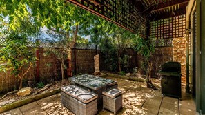 Un patio al aire libre con mobiliario de mimbre, pared de piedra y zona de barbacoa.