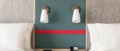 Una habitación de hotel con dos camas, una mesita de noche con un reloj digital, un teléfono y dos lámparas de pared.