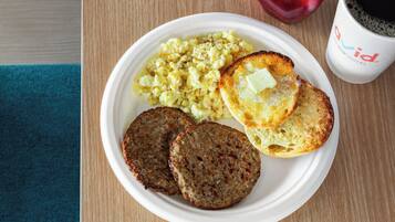 A plate with scrambled eggs, toast with butter, and two patties, accompanied by a coffee cup and a red apple on a wooden table.
