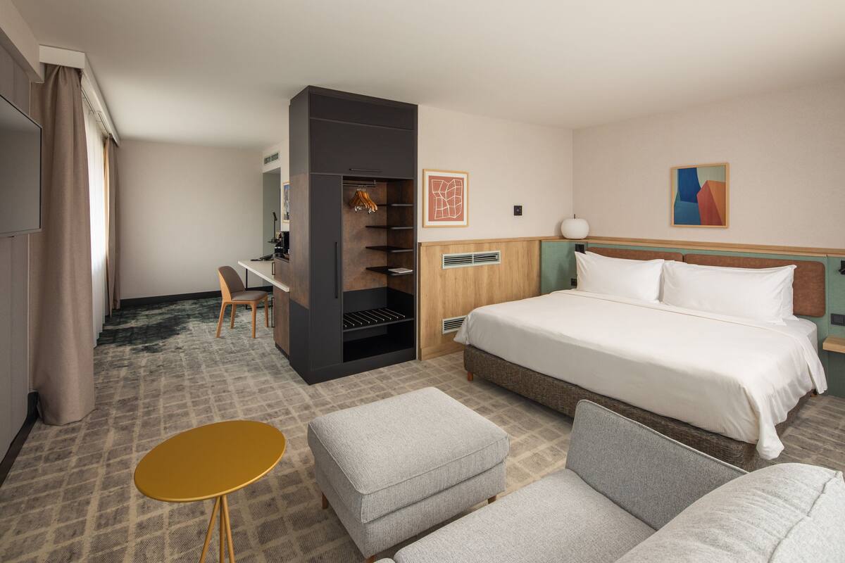 A hotel room with a bed, a desk, a chair, and a small table.