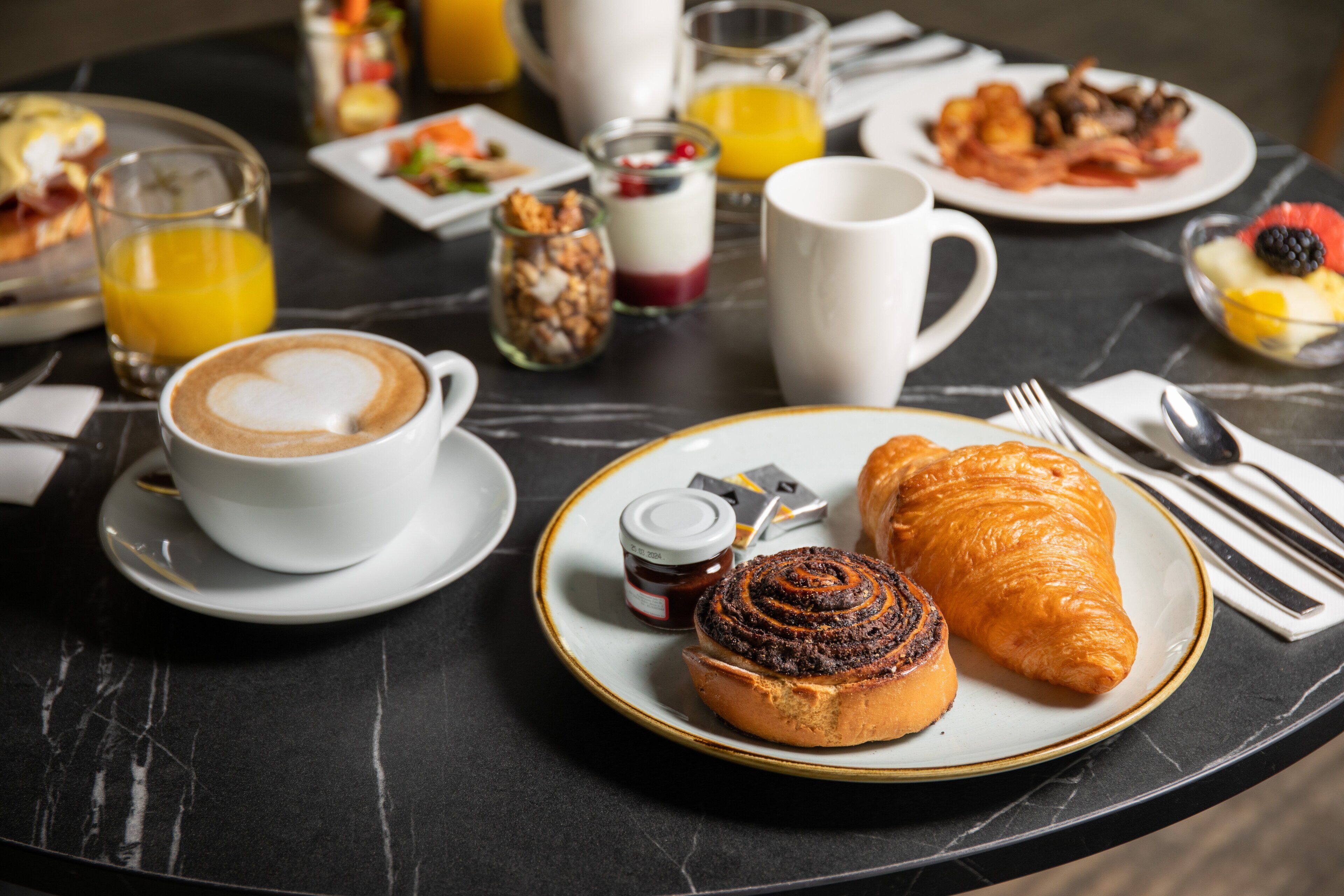 Un desayuno con croissants, una taza de café y diversas opciones sobre una mesa de mármol.