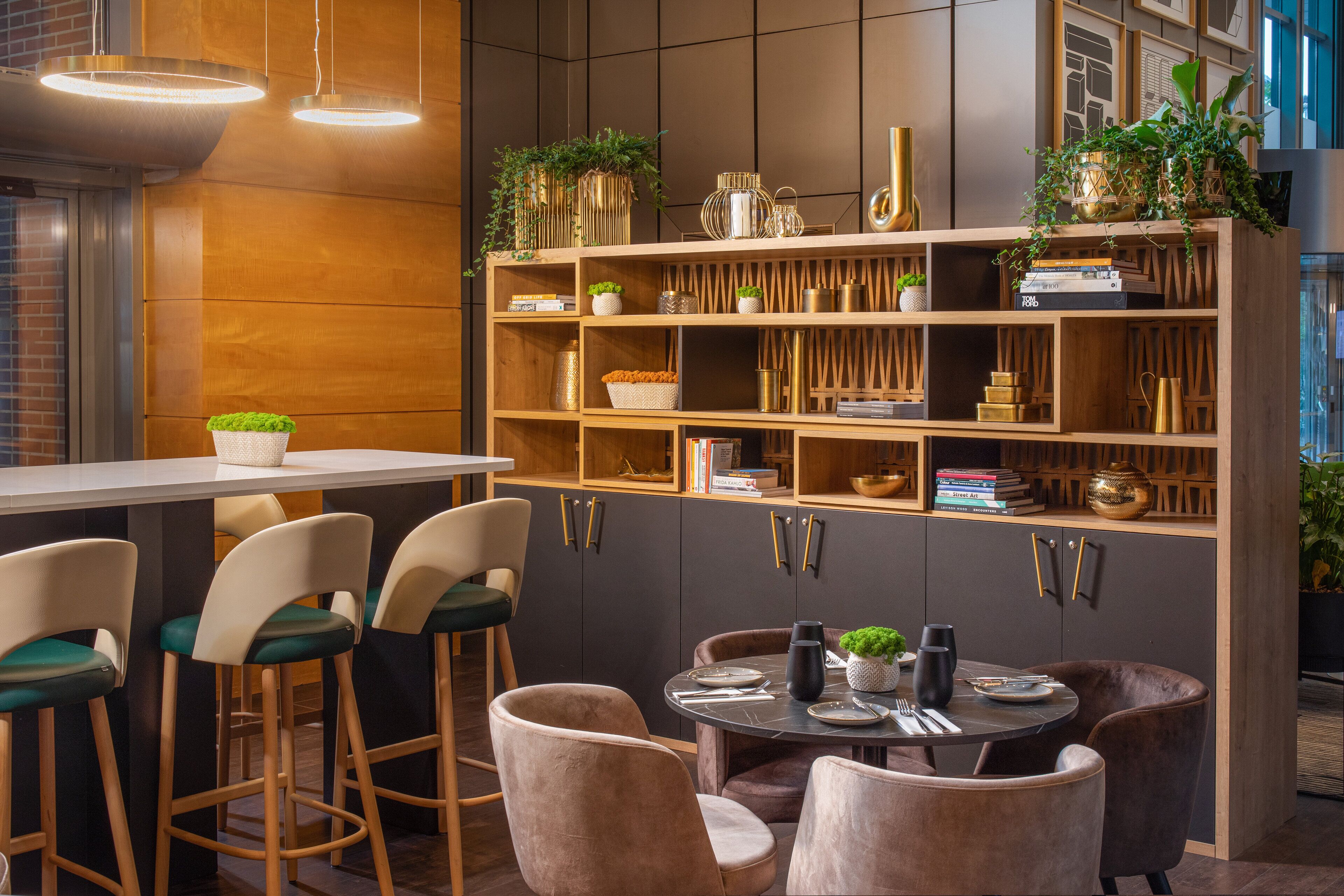 Una cocina moderna con barra de madera y taburetes, una mesa de comedor redonda y una estantería empotrada con objetos decorativos.