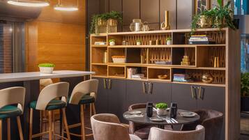 Una cocina moderna con barra de madera y taburetes, una mesa de comedor redonda y una estantería empotrada con objetos decorativos.