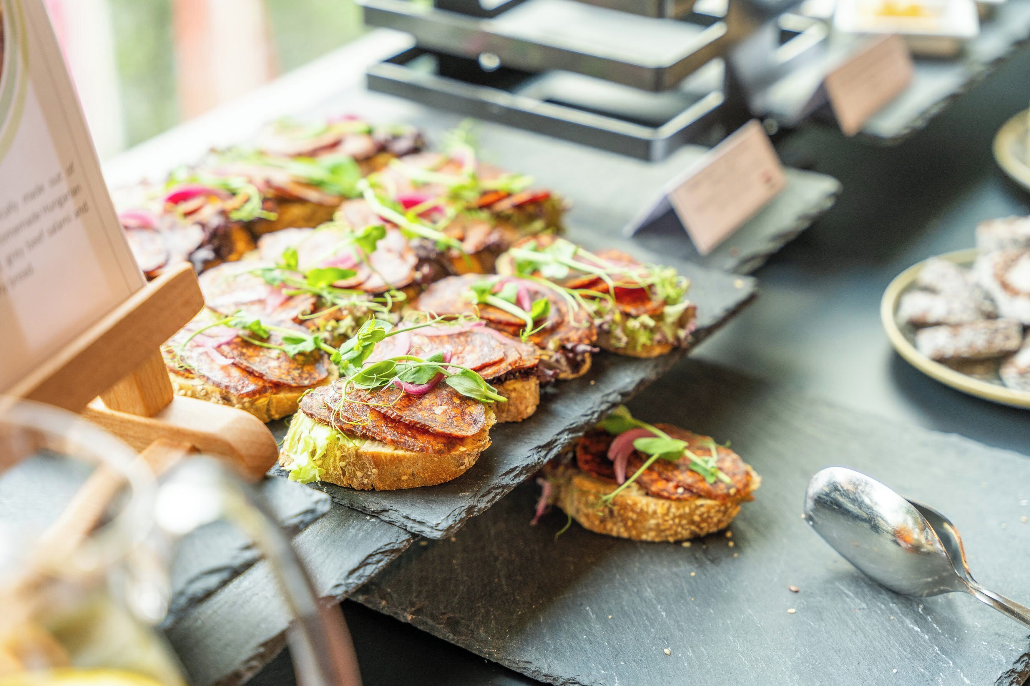 A buffet table with various food items, including sandwiches and pastries, on a slate serving board.