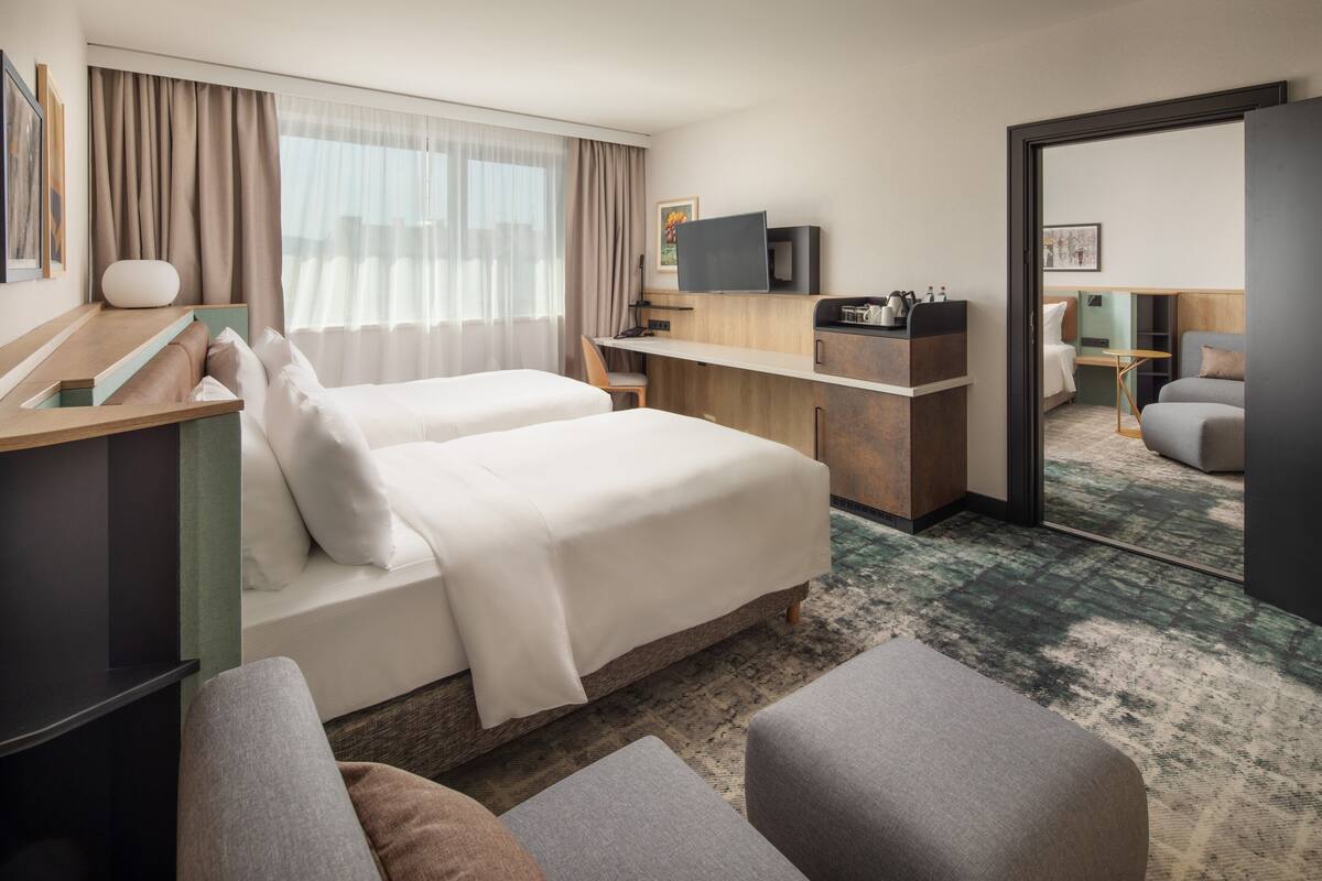 A hotel room with two beds, a desk, a TV, and a mirror.