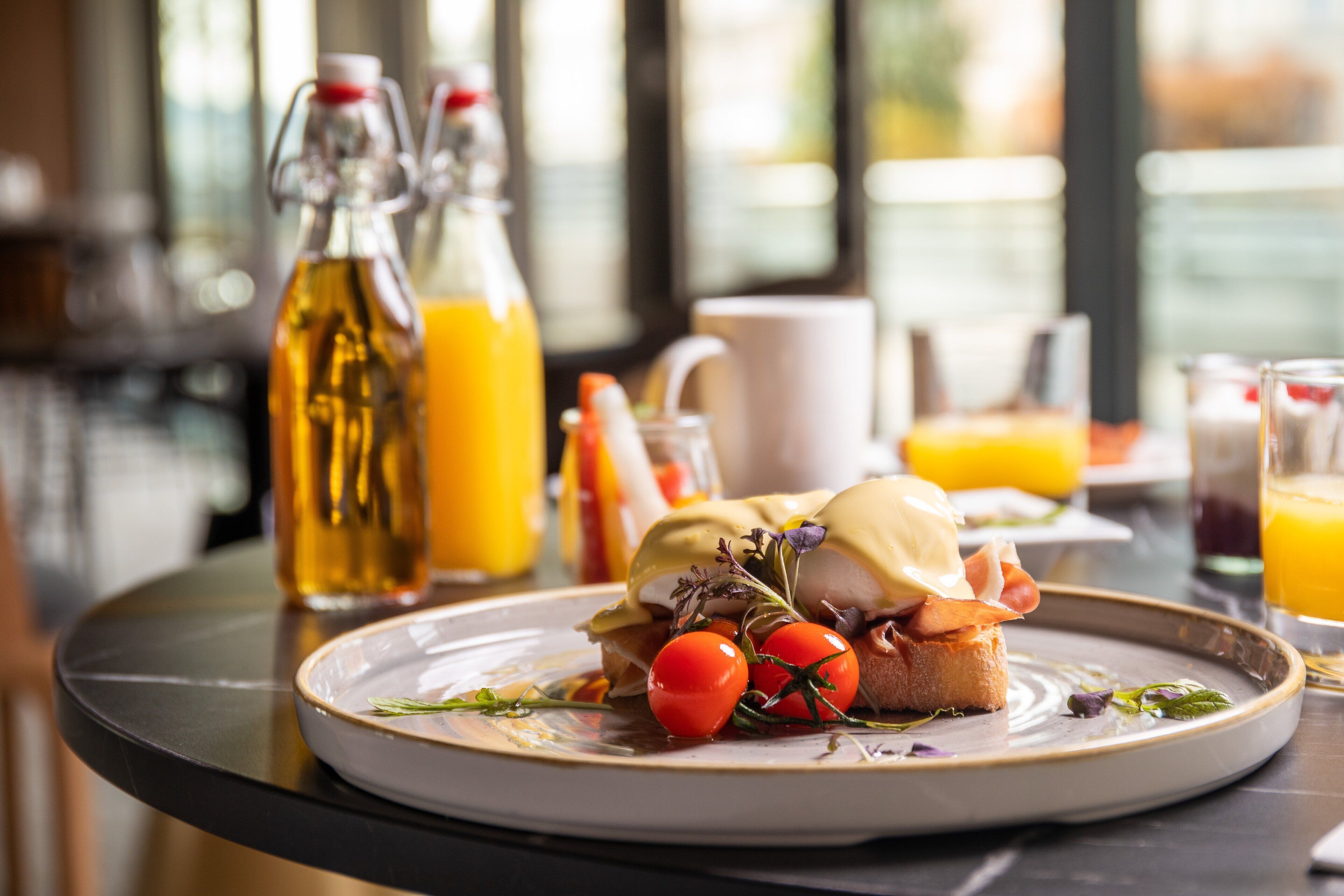 A breakfast plate with eggs, tomatoes, and greens on a table with a bottle of orange juice and a glass of orange juice.