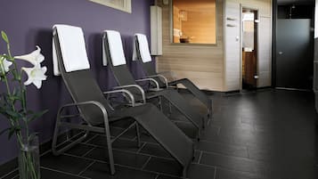 Varias sillas de masaje en un área de spa con suelo de baldosas y pared de madera.