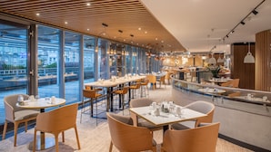 A modern restaurant with a wooden ceiling, large windows, and a view of buildings outside. - Crowne Plaza Budapest by IHG (Budapest)
