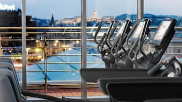 A row of stationary exercise bikes with digital displays, positioned in front of a large window overlooking a cityscape.