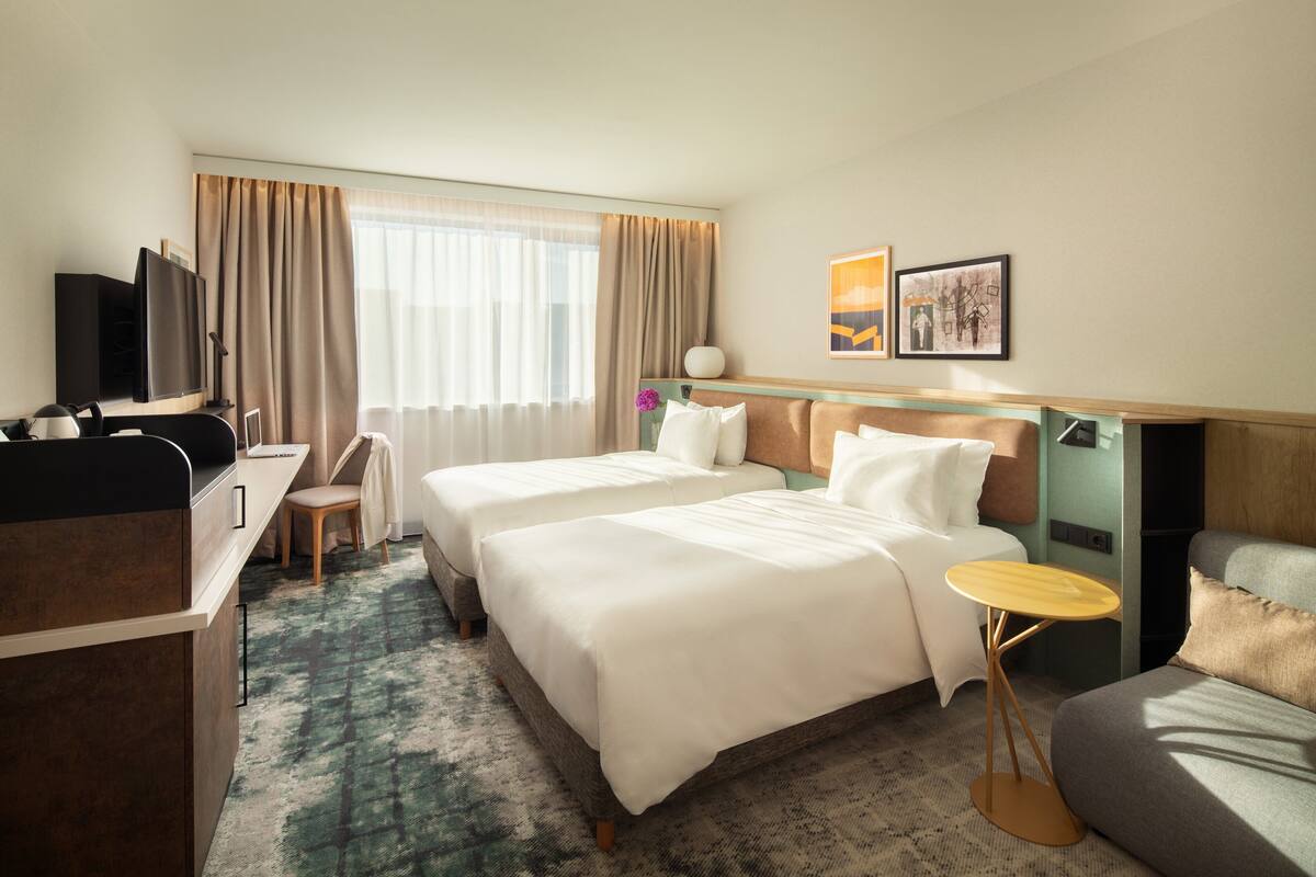 A hotel room with two beds, a desk, a TV, and a small table.