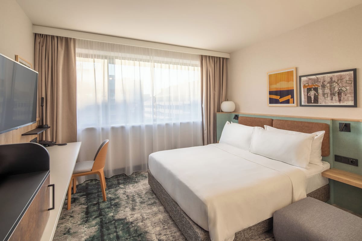 Une chambre d’hôtel avec un lit, un bureau et une chaise, une télévision et des œuvres d’art accrochées au mur.