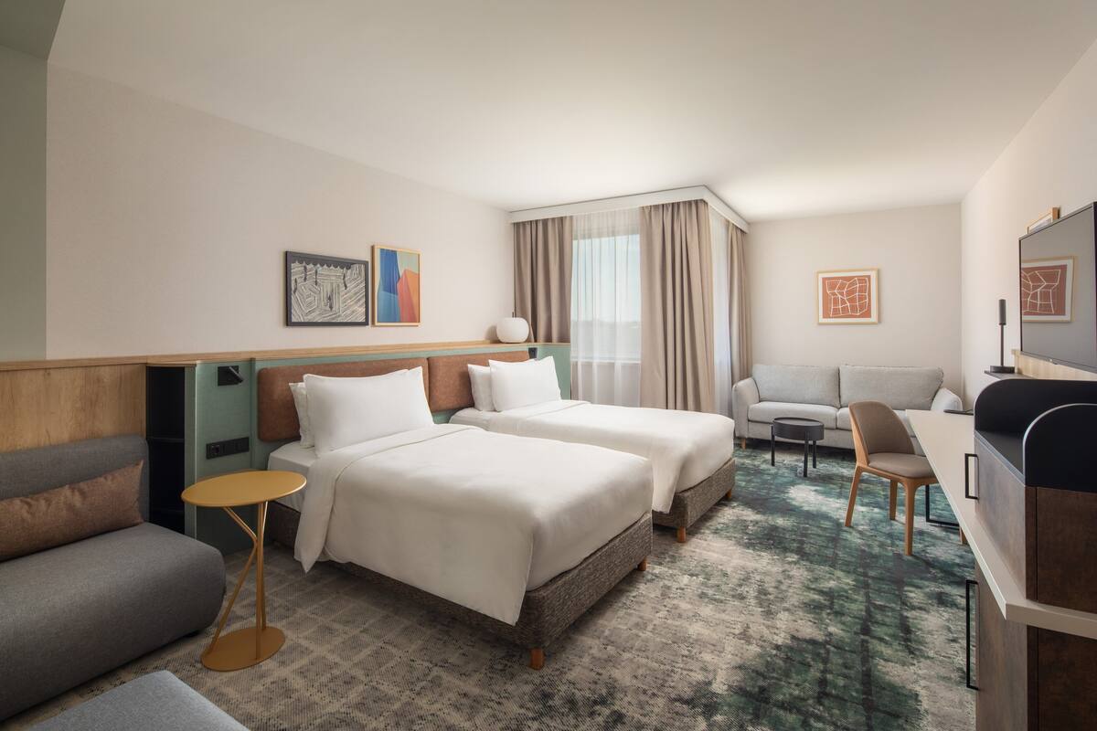 A hotel room with two beds, a sofa, a small round table, a desk, and a TV.
