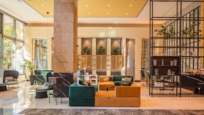A modern lobby with a large central pillar, seating areas, a reception desk, and a bookshelf. - Crowne Plaza Budapest by IHG (Budapest)
