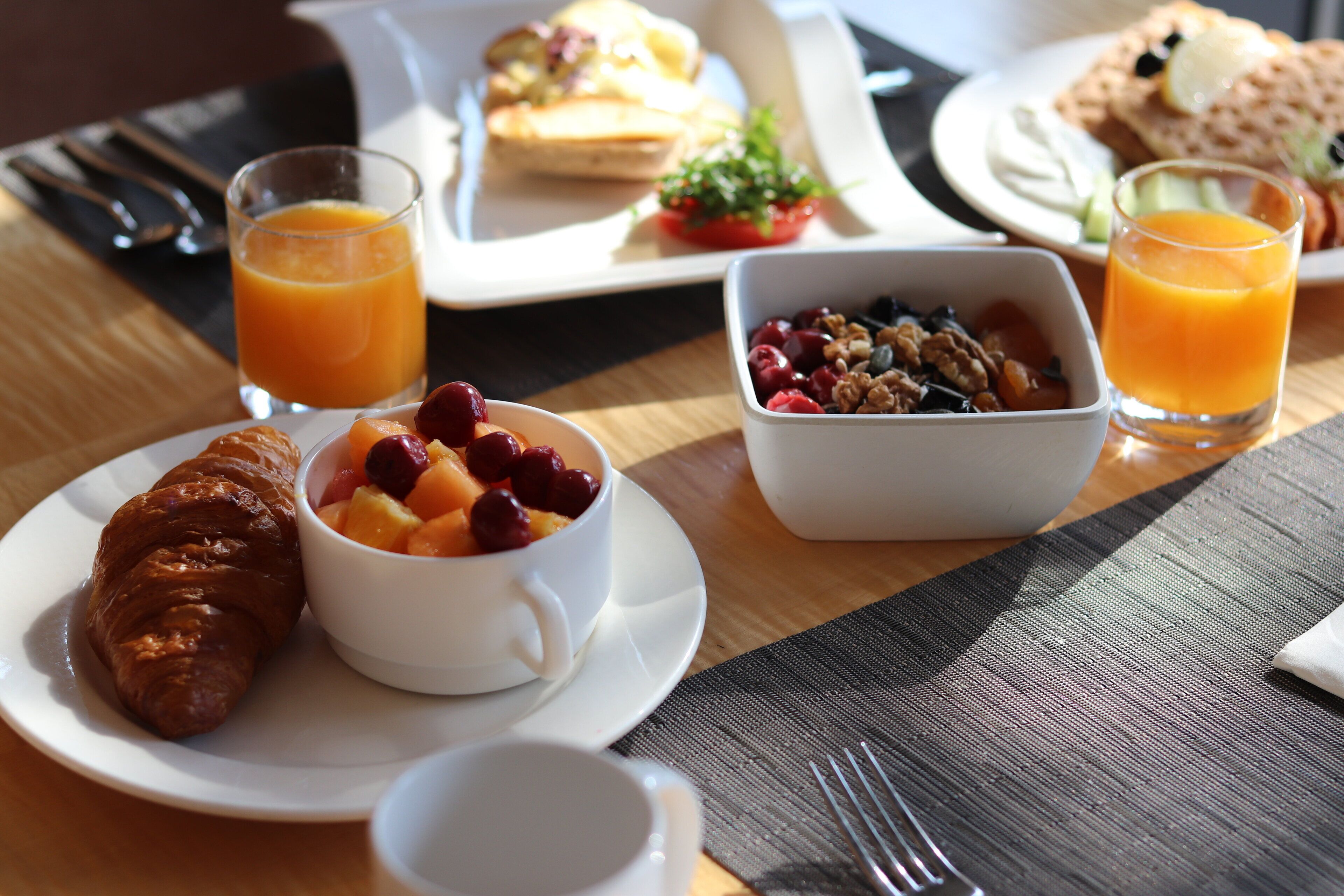 A breakfast setting with croissants, fruit, granola, and orange juice on a wooden table.