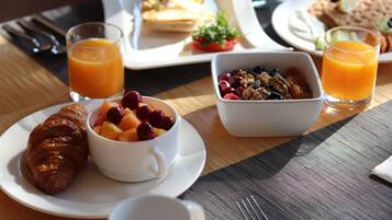 A breakfast setting with croissants, fruit, granola, and orange juice on a wooden table.