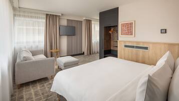 Quarto de hotel com cama grande, sofá, televisão, cabideiro e guarda-roupa.