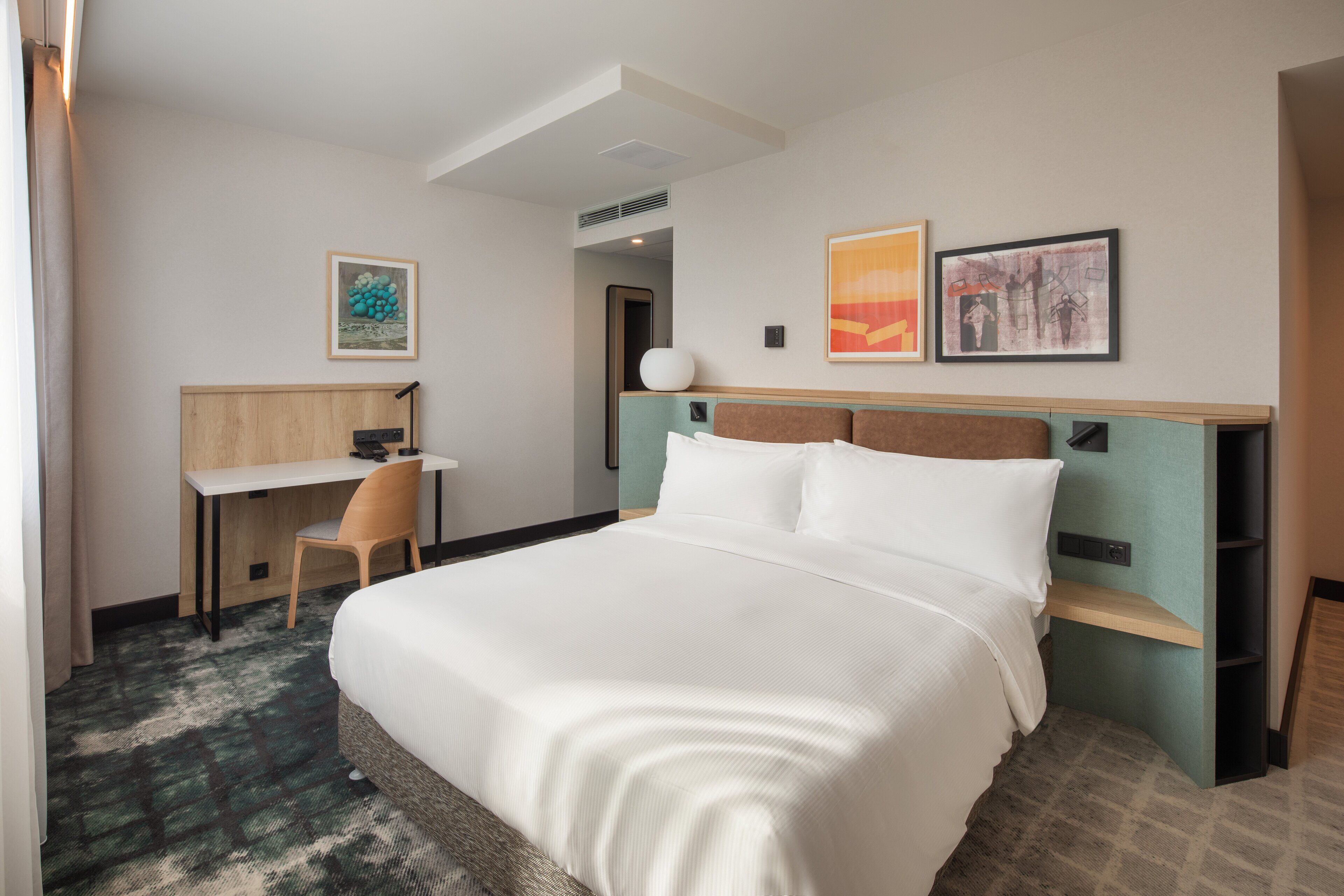 A hotel room with a large bed, a desk, and two chairs. There are two framed pictures on the wall.