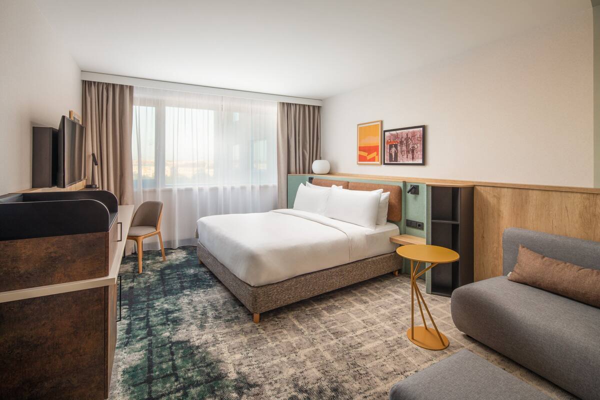 A hotel room with a bed, a sofa, a desk, and a TV.