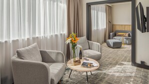 A modern hotel room with two grey sofas, a coffee table with a vase of flowers, a bottle of wine, and a magazine. - Crowne Plaza Budapest by IHG (Budapest)
