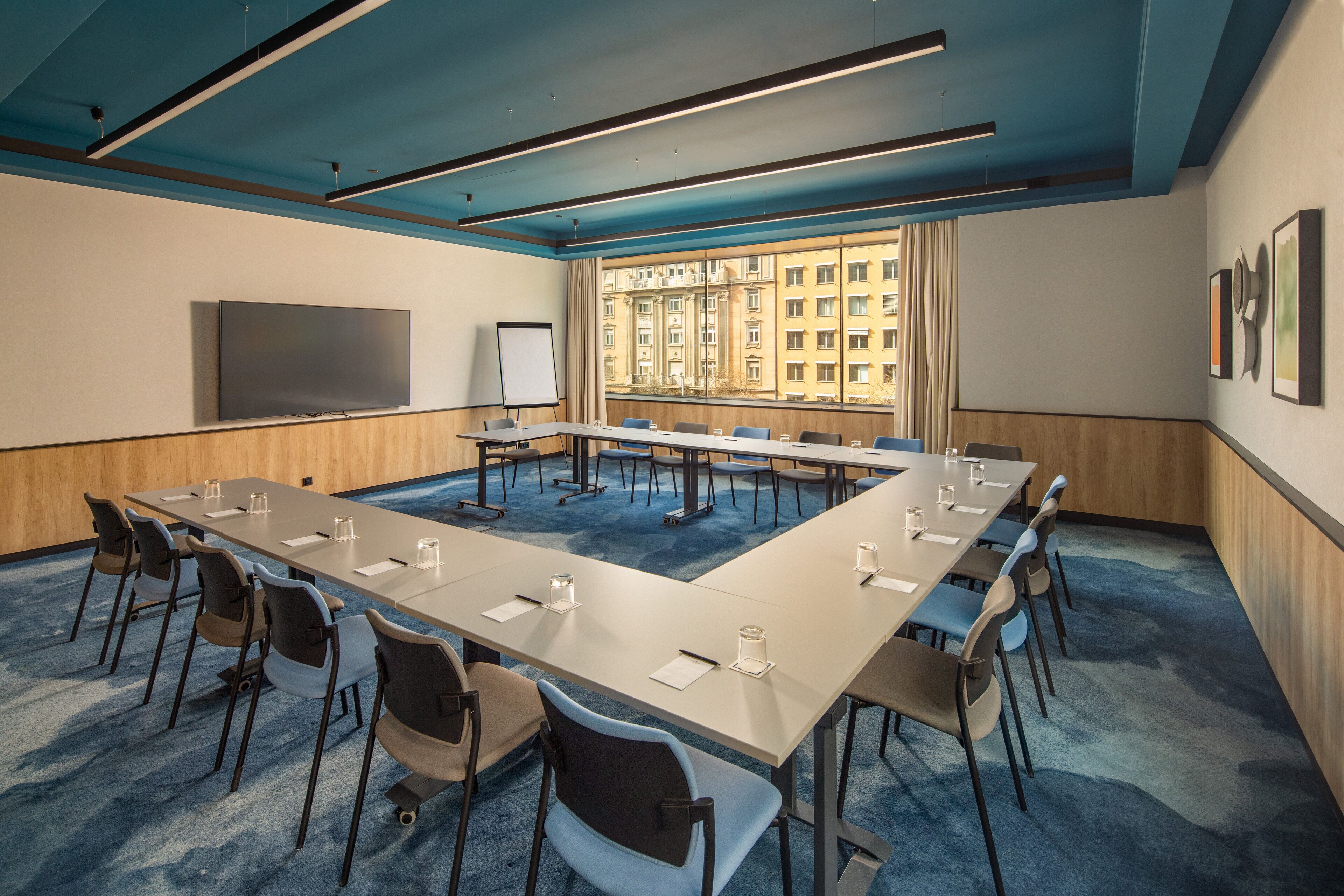 Uma sala de conferências com uma mesa comprida, cadeiras, um quadro branco e uma janela grande com vista para a cidade.