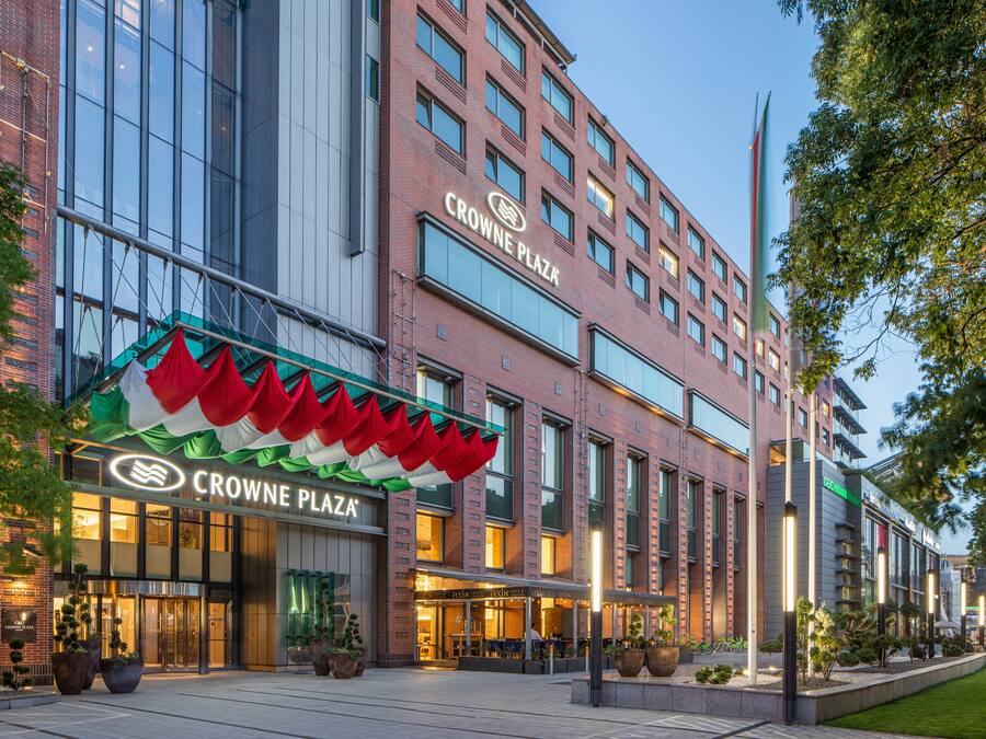 Un hotel con un letrero llamativo, ventanas amplias y un área exterior bien cuidada con plantas en macetas.