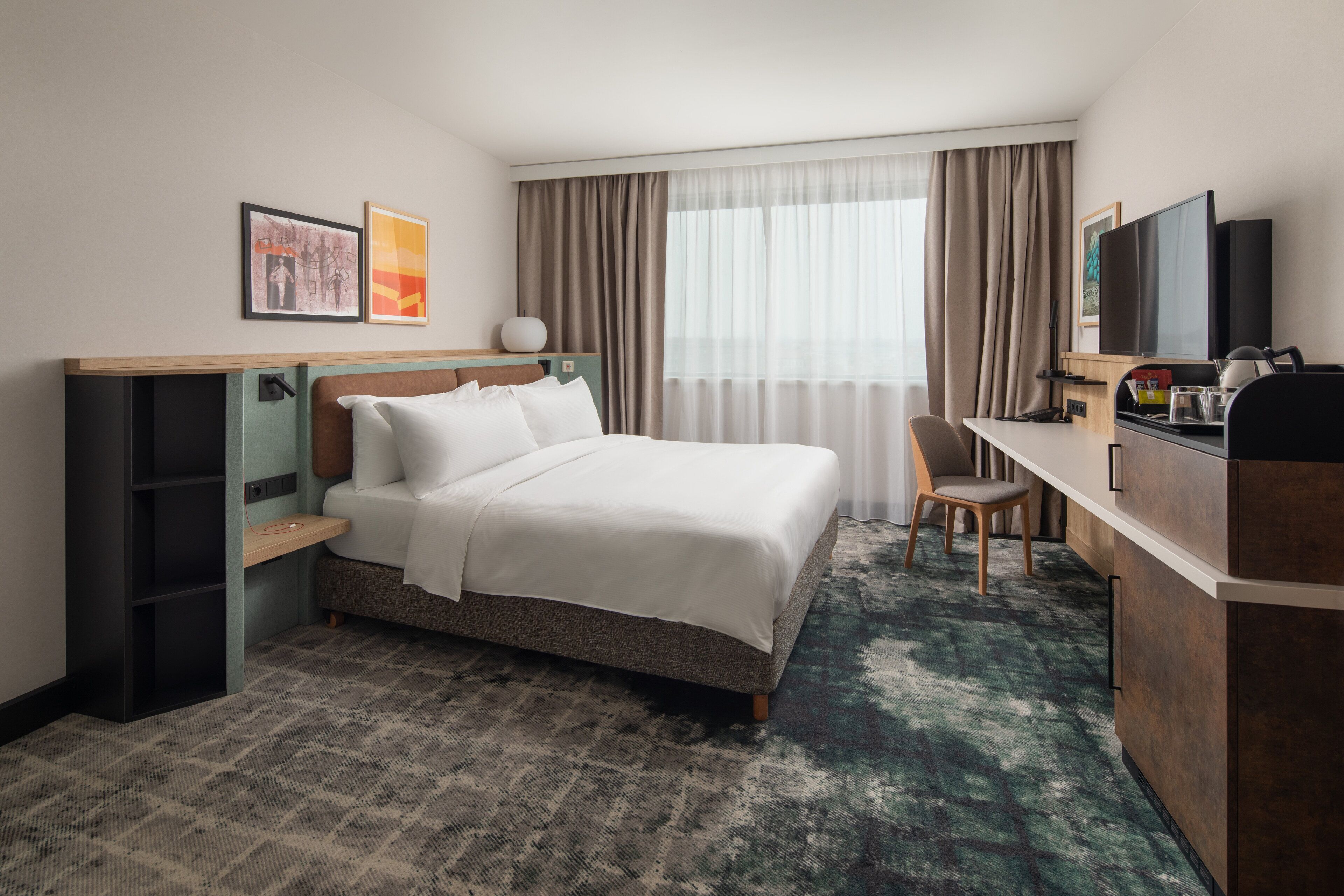 A hotel room with a bed, a desk, a chair, a television, and a window with curtains.
