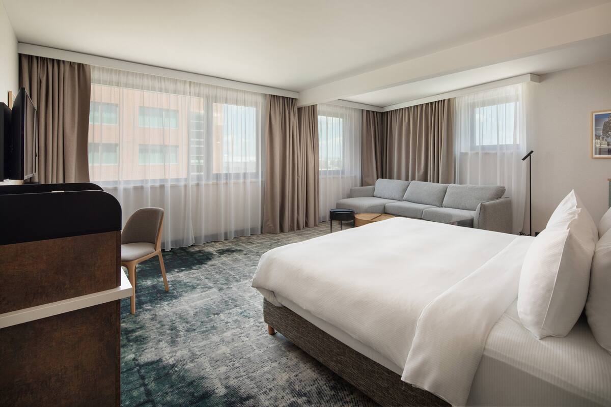 A hotel room with a large bed, a sofa, a chair, a desk, and a television.