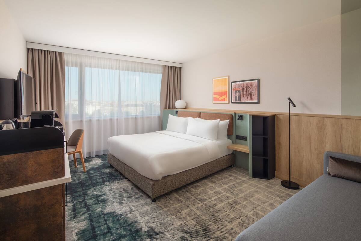 A hotel room with a large bed, a desk with a computer, a chair, and a TV.