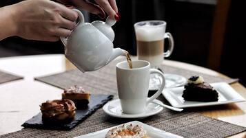A person pouring coffee into a cup, with pastries on plates and a mug in the background.