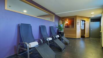 A reception area with a purple wall, three reclining chairs with white cushions, a wooden reception desk, and a potted plant.
