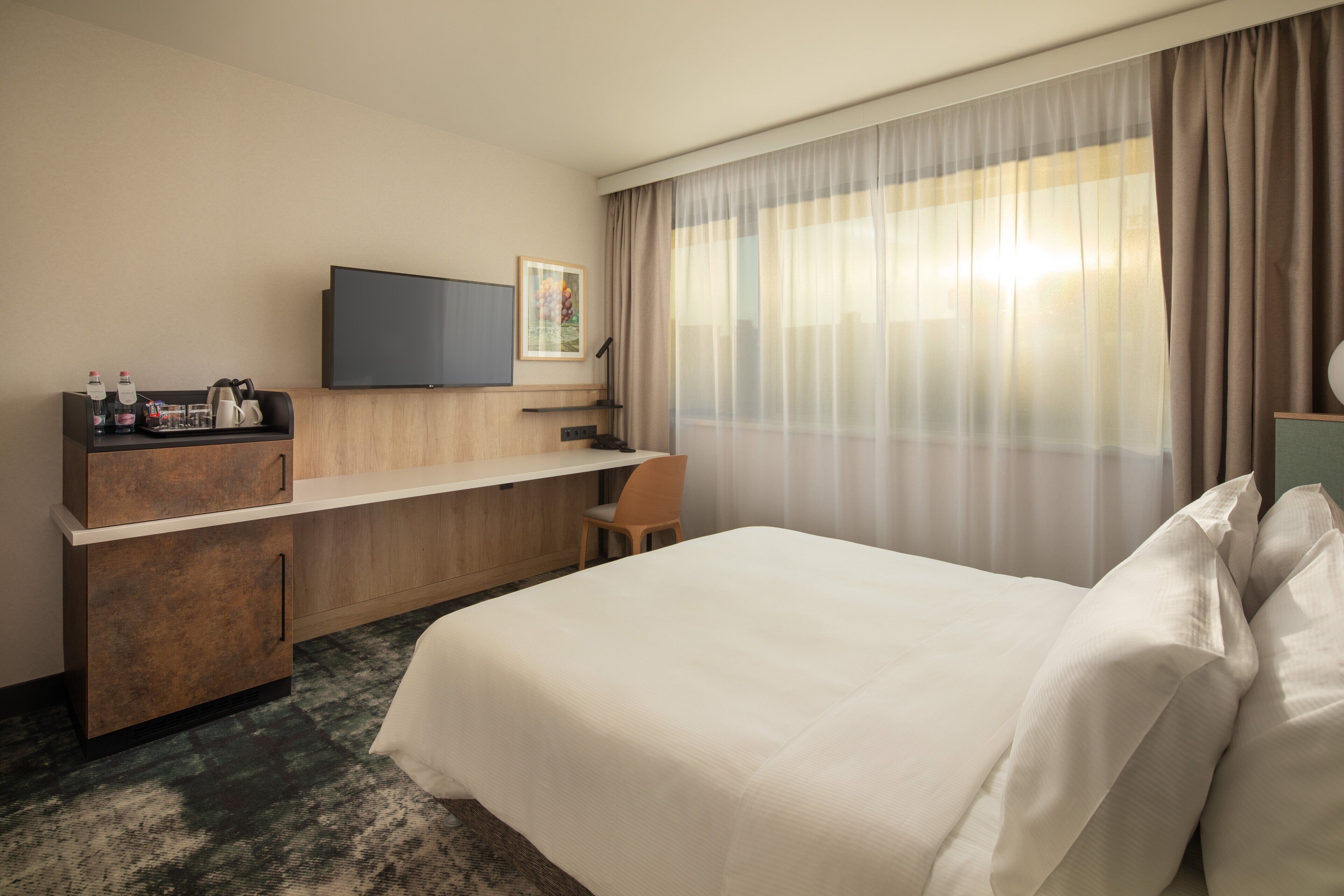 A hotel room with a bed, a desk, a television, and a window with curtains.