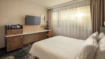 A hotel room with a bed, a desk, a television, and a window with curtains.