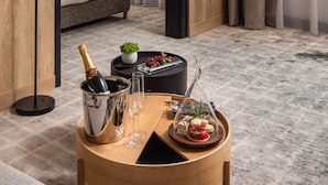 A hotel room with a bed, a bedside table with a bottle of champagne, glasses, a tray with snacks, and a view of the outside through sheer curtains. - Crowne Plaza Budapest by IHG (Budapest)