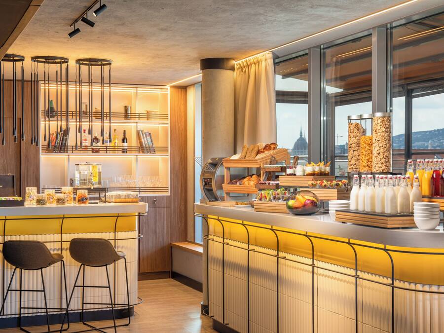 Zona moderna de bar con mostrador, taburetes y diversas opciones de comida y bebida.