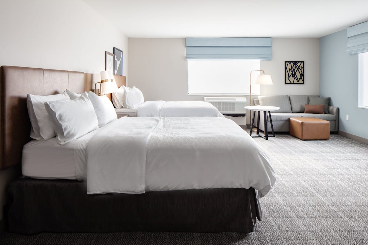 Une chambre d’hôtel avec un grand lit, un canapé, une petite table et une fenêtre avec des stores.