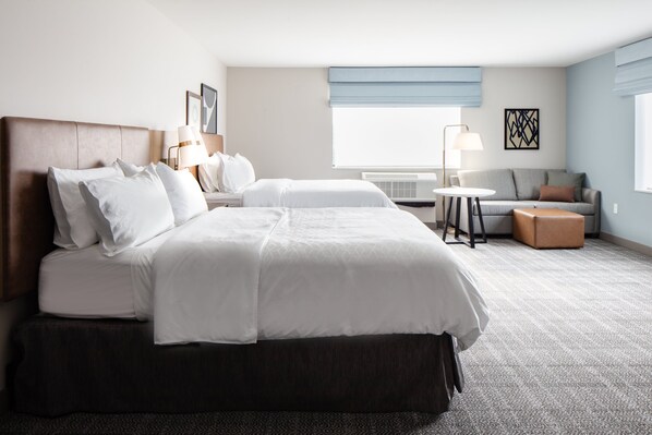 Quarto de hotel com uma cama grande, um sofá, uma mesinha e uma janela com persianas.