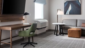 Habitación de hotel con televisor de pantalla plana, escritorio con silla, sofá, una pequeña mesa redonda y una lámpara.