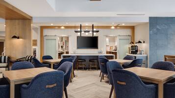 A modern dining area with a central bar, multiple seating arrangements, and a large flat-screen TV mounted on the wall.
