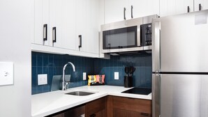 Una cocina moderna con armarios blancos, un refrigerador de acero inoxidable, un microondas y un lavamanos.