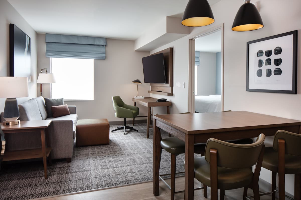 Une chambre d’hôtel moderne équipée d’un canapé, d’une table à manger, d’un téléviseur et d’un tableau encadré au mur.