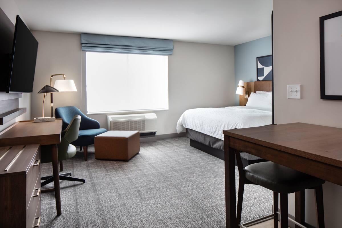 Une chambre d’hôtel équipée d’un lit, d’un bureau, d’une chaise, d’une télévision et d’une fenêtre donnant sur un paysage agréable.