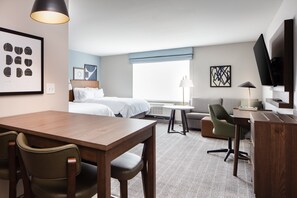 Una habitación de hotel con una mesa de comedor de madera, dos camas individuales, un sofá, un televisor y un escritorio pequeño con una silla.