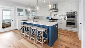 A modern kitchen with white cabinets, a blue island, and stainless steel appliances. - Expansive Bayfront Home w/ Heated Saltwater Pool & Dock (Ship Bottom)