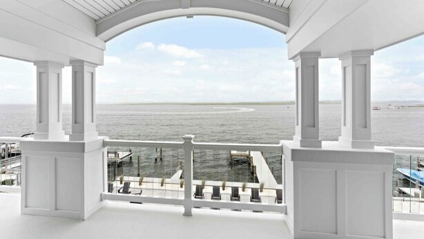 A covered balcony with a view of the sea and a pier. - Expansive Bayfront Home w/ Heated Saltwater Pool & Dock (Ship Bottom)
